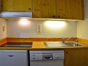 A compact kitchen with wooden cabinets, a built-in dishwasher, a sink, and a range hood.