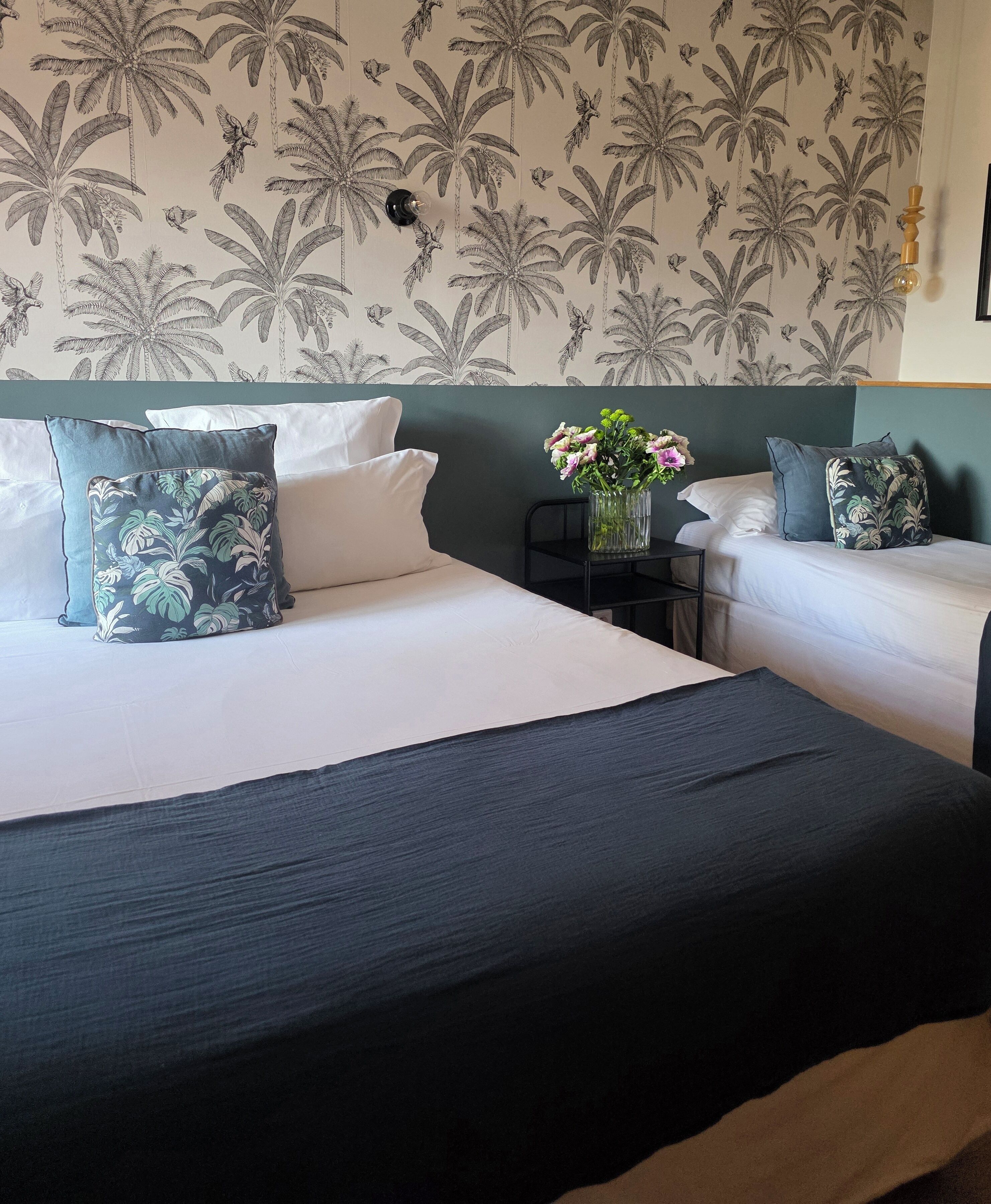 A hotel room with two beds, a nightstand, and a wall with a tropical plant pattern.