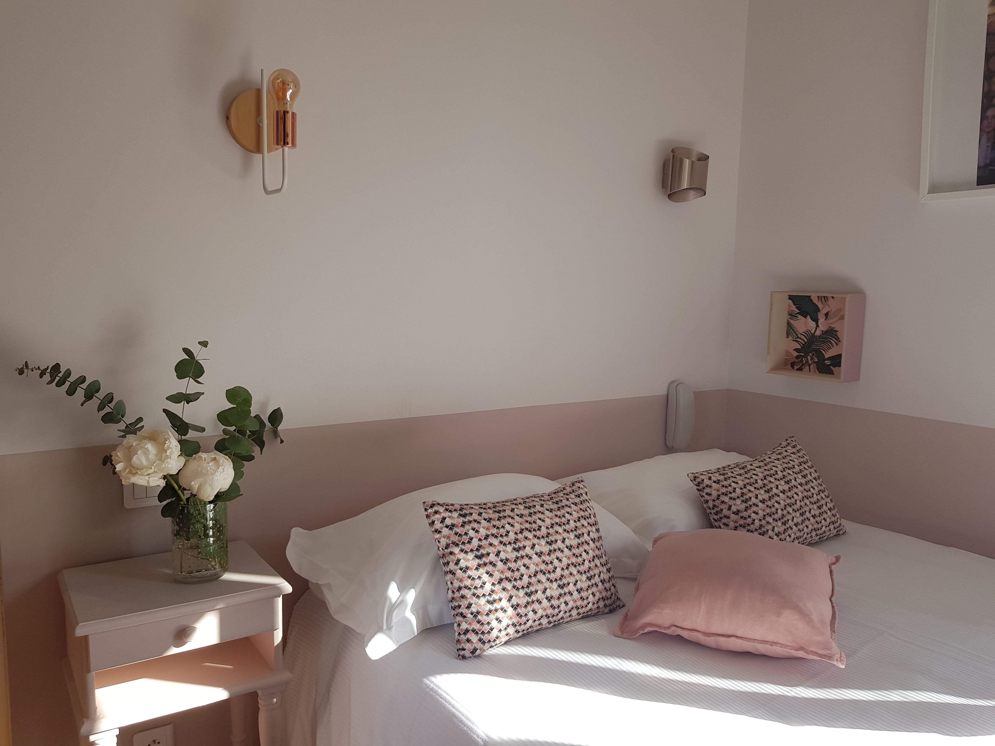 A bedroom with a bed, bedside table, and a wall-mounted light fixture.