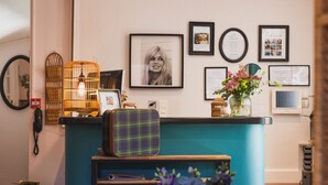 Un mostrador de recepción con una encimera verde, cuadros en la pared, una jaula de mimbre con luz y una pequeña mesa con un florero.