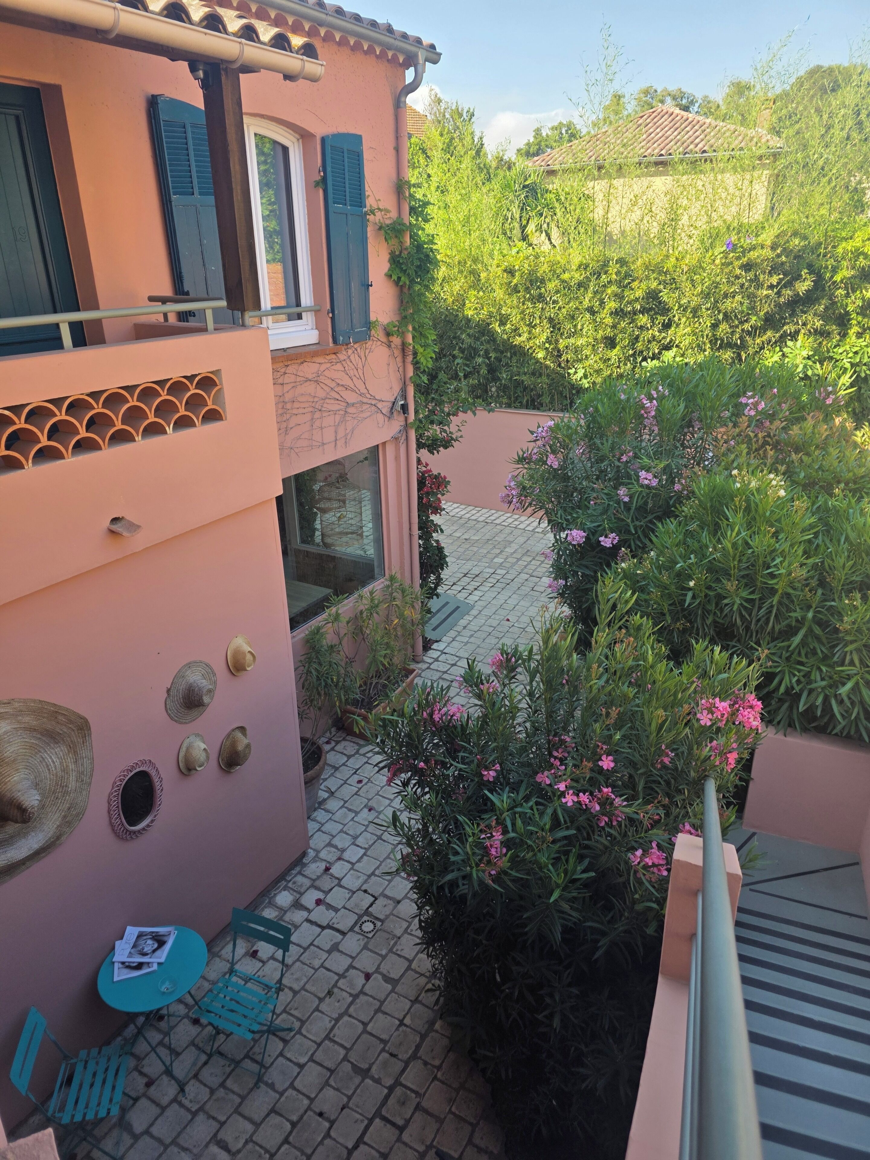 A courtyard with a pink building, a tiled floor, and potted plants with pink flowers.