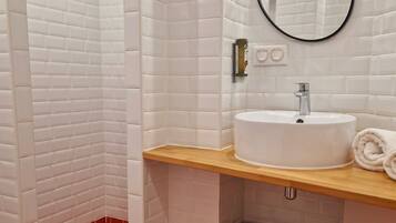 A bathroom with white subway tile walls, a white sink with a mirror, and a red-tiled floor.