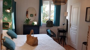 Un dormitorio con cama, cómoda, silla, escritorio, lámpara colgante y ventana con cortinas.