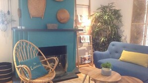 Una sala de estar con un sofá azul, una silla de mimbre, una mesa redonda de madera y una chimenea.