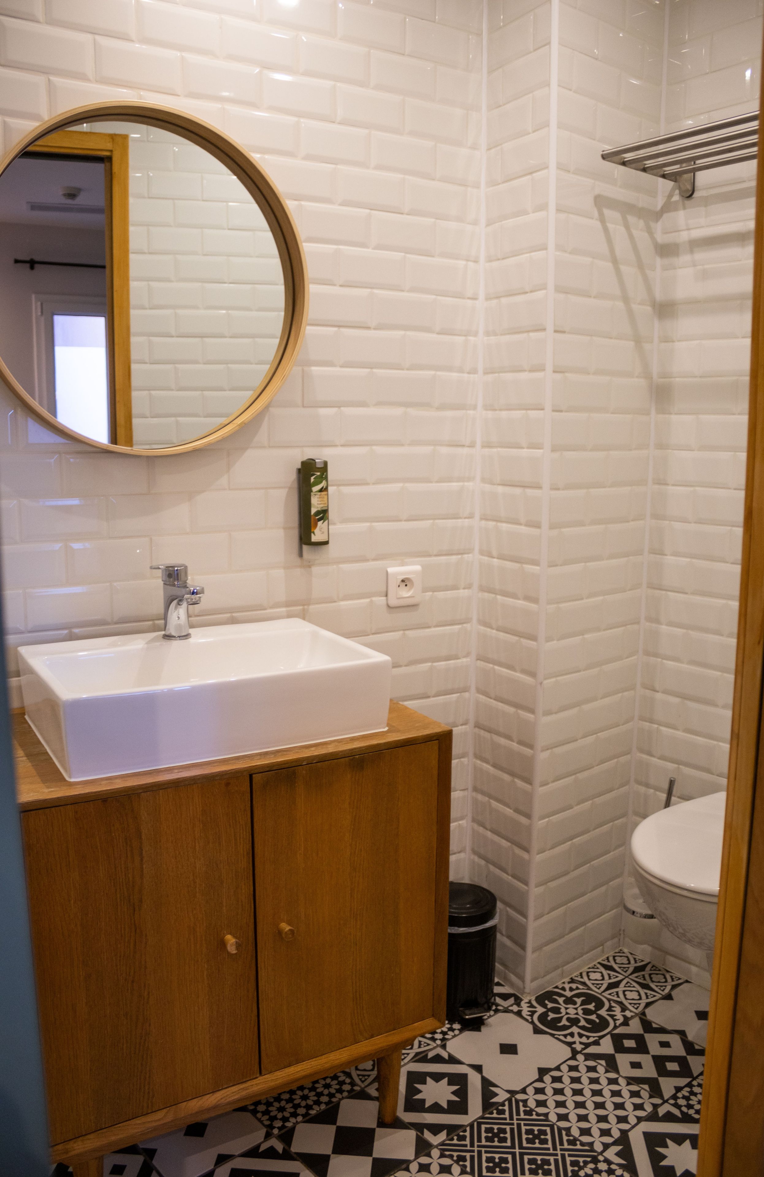 Un baño con un lavamanos blanco, un mueble de madera y un espejo redondo.