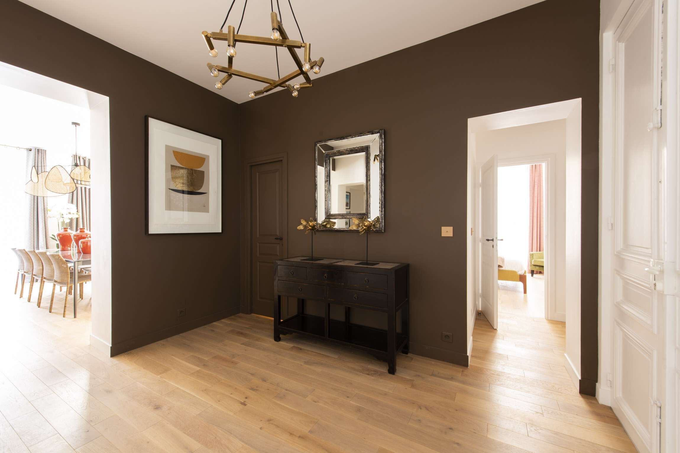 Una habitación amplia con piso de madera, una consola negra, un espejo grande y una obra enmarcadas en la pared.