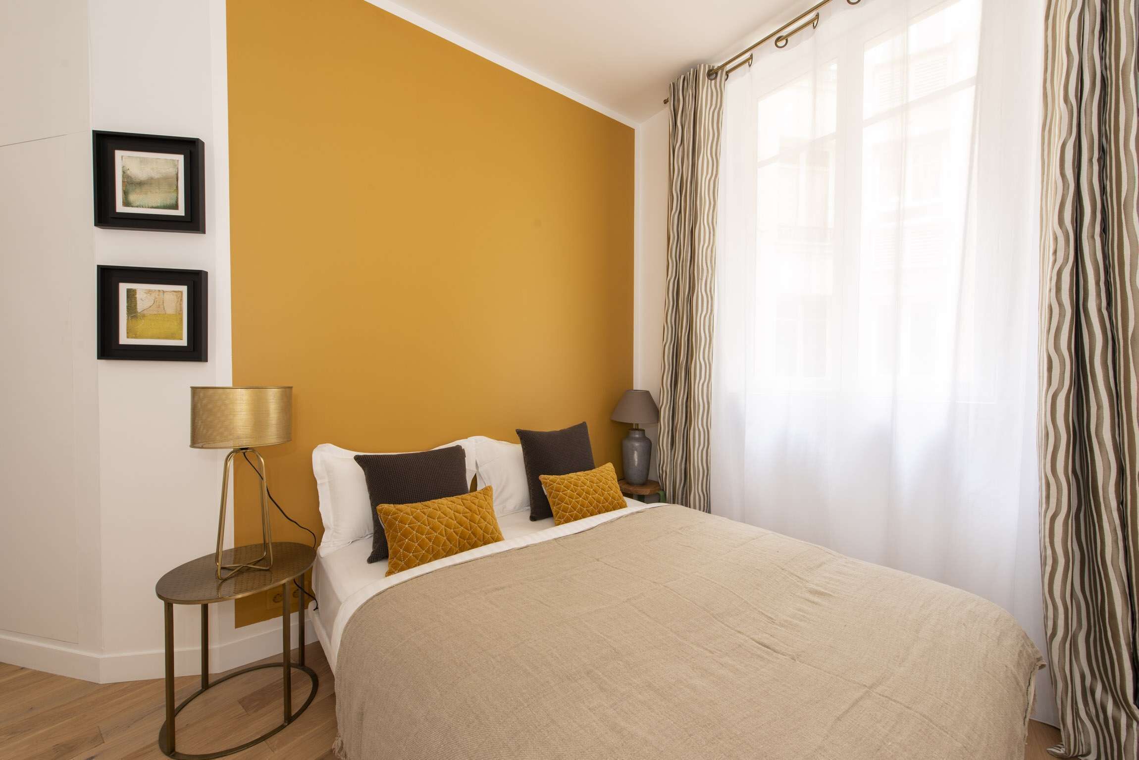 A bedroom with a large bed, two bedside tables, a lamp, and a view of the outdoors through sheer curtains.