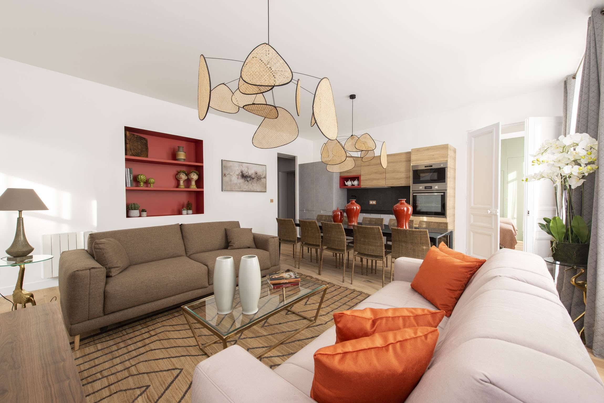 Ein modernes Wohnzimmer mit Sofa, Couchtisch und Dekoration. Es gibt einen Essbereich mit Stühlen und einem Tisch. Der Raum hat eine neutrale Farbgestaltung und ein großes Fenster.