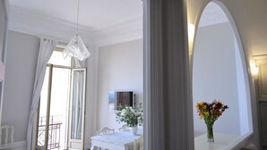 A hotel room with a dining area, a TV mounted on the wall, and a vase with flowers on the table.