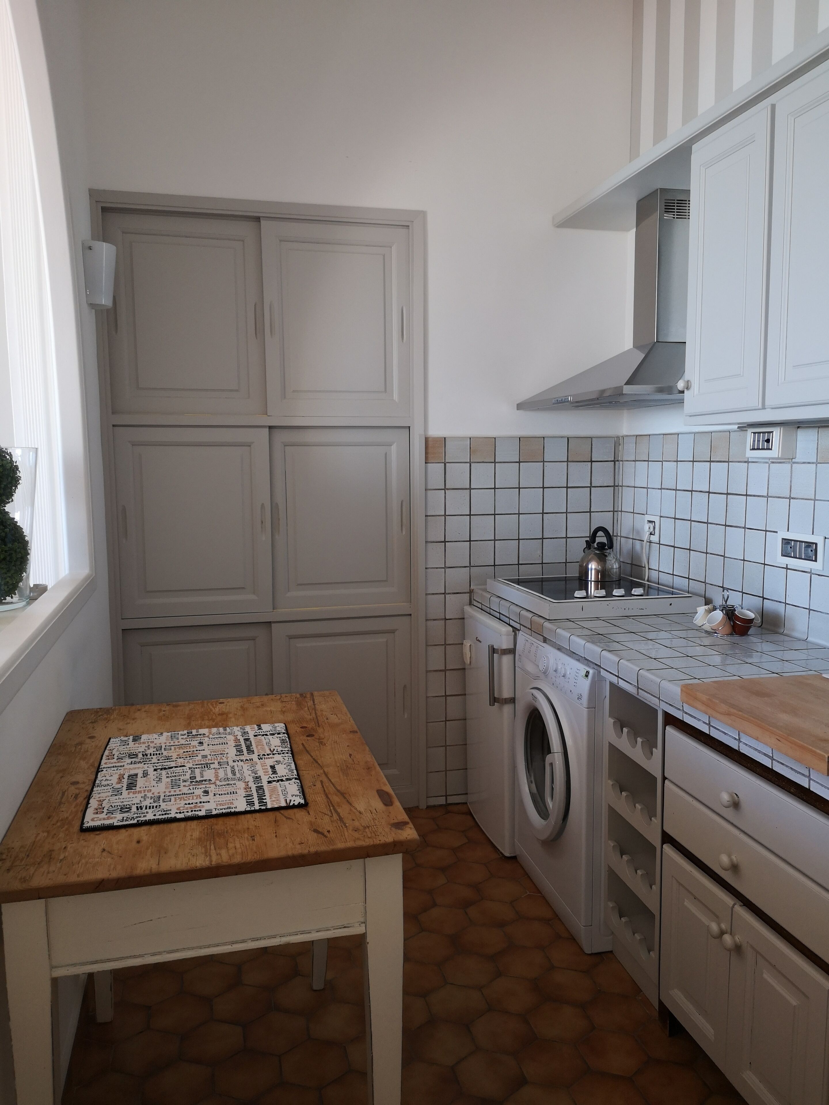 Uma cozinha compacta com máquina de lavar, uma mesa de madeira e painel de azulejos.