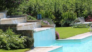 Une piscine agrémentée d’une cascade en pierre, entourée d’une pelouse bien entretenue et de diverses plantes.
