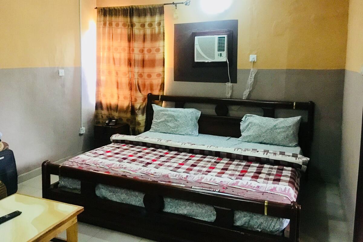 Un dormitorio con cama, mesita de noche, mesa y un equipo de aire acondicionado instalado en la pared.