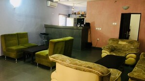 A living room with green and beige armchairs, a small table, and a bar area with bottles. - Cossy Hotel & Suite (Agbor)
