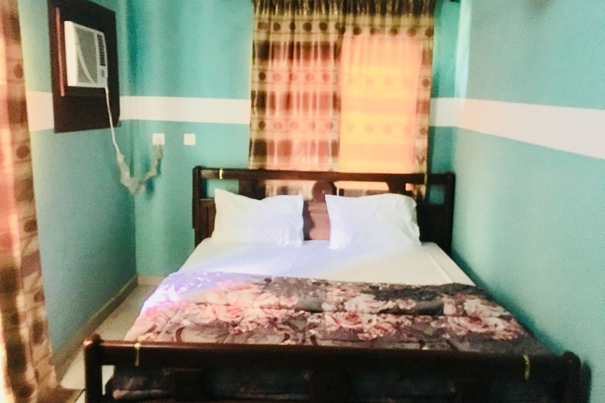 Una cama con una colcha estampada con flores, un cabecero de madera y una cortina.