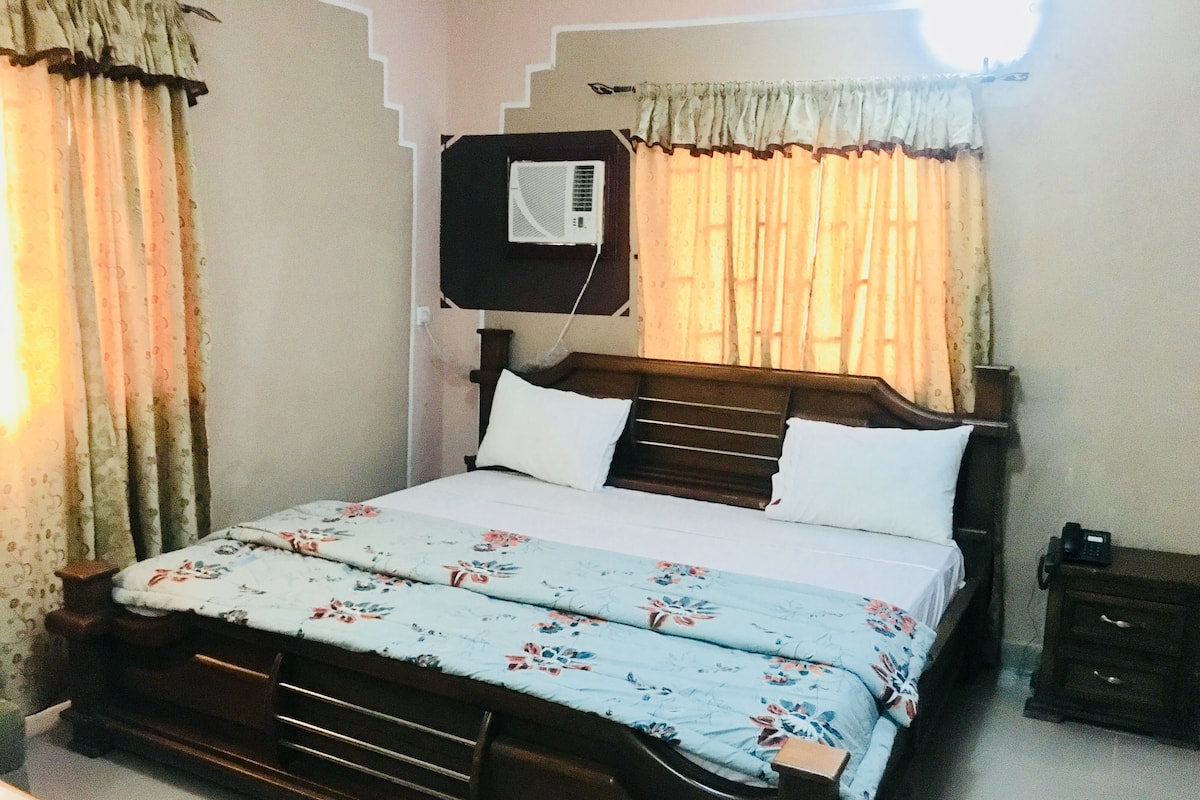 Un dormitorio con cama de madera, ropa de cama floral, aire acondicionado de pared y cortinas.
