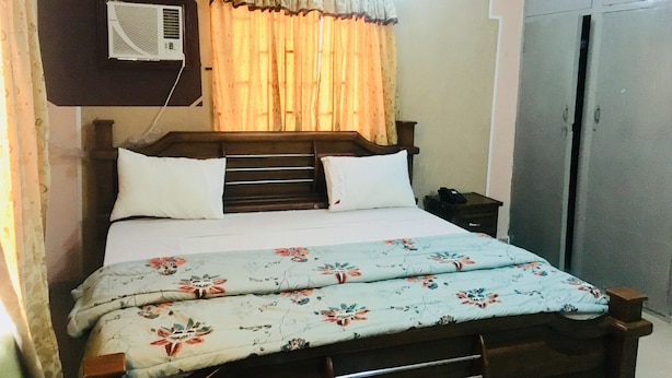 A bed with a floral bedspread, a wooden headboard, and a nightstand with a phone. - Cossy Hotel & Suite (Agbor)