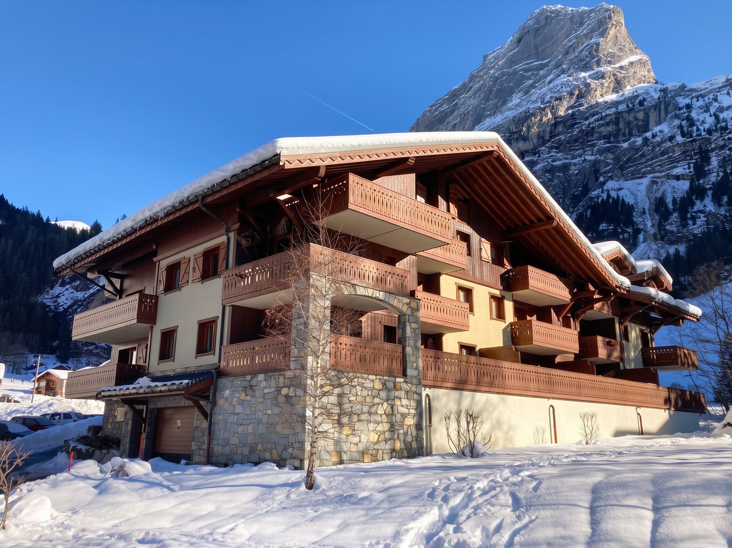 A multi-story chalet with balconies, stone foundation, and a mountain backdrop.