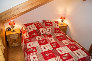 Une chambre confortable avec un plafond en pente, une couvre-lit matelassé, deux lampes de chevet et une table de chevet en bois avec une horloge.