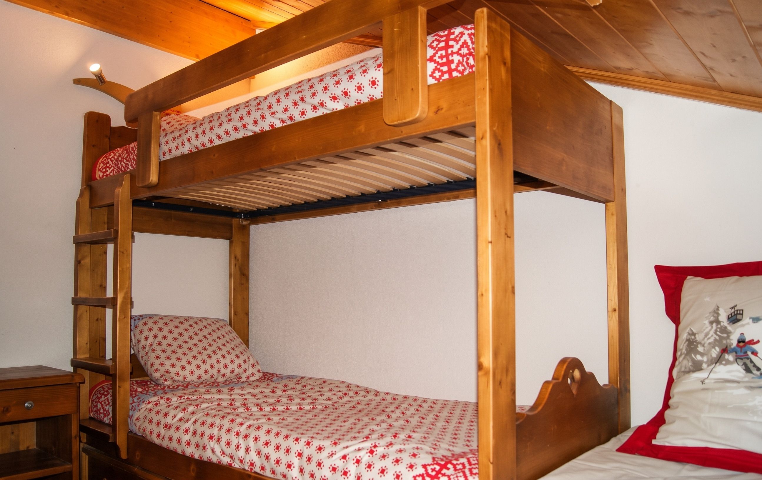 Ein Stockbett mit einer Leiter, ein kleiner Holztisch und ein Kissen mit einer Darstellung von Skifahren.