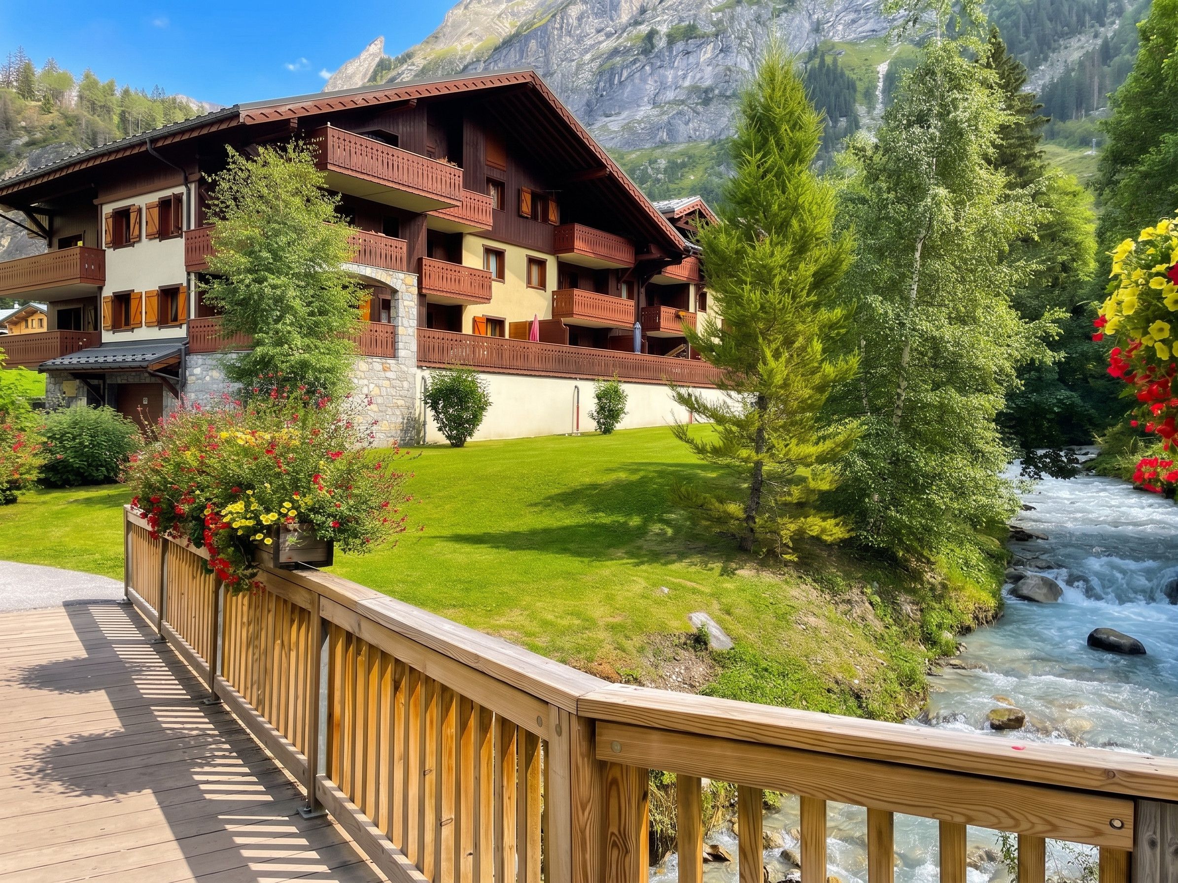 Un hôtel de style chalet doté de balcons, d’une terrasse en bois et offrant une vue sur la rivière.