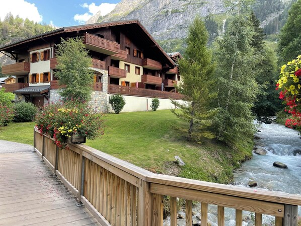 Ein Chalet mit mehreren Balkonen, einer Holzterrasse und einem Fluss im Hintergrund.