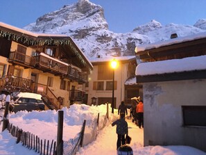 Eine verschneite Straße mit Gebäuden, ein Berg im Hintergrund und eine Straßenlaterne.