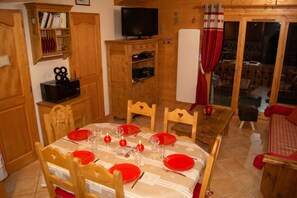 A dining area with a table set for four, wooden chairs, and a television above the table. - Homerez - Apartment in Pralognan with balcony (Pralognan-la-Vanoise)