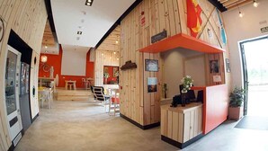 Un moderno hall de hotel con paneles de madera, una mesa de recepción y un comedor con mesas y sillas.