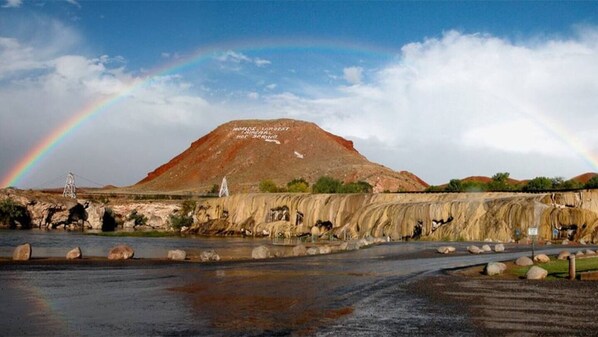 A large hill with a rainbow, a river, and a road with rocks.