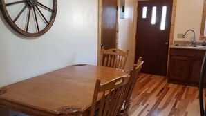 A dining area with a wooden table and chairs, a wooden floor, and a wall-mounted wheel. - Furnished with a western decor and many antiques, yet has modern amenities. (Thermopolis)