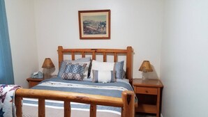 A bedroom with a wooden bed, two bedside tables with lamps, a framed picture on the wall, and a patterned throw on the bed. - Furnished with a western decor and many antiques, yet has modern amenities. (Thermopolis)