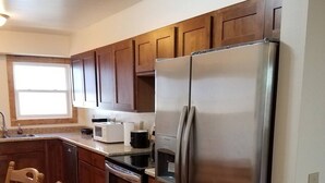 A kitchen with wooden cabinets, a stainless steel refrigerator, a microwave, and a stove. - Furnished with a western decor and many antiques, yet has modern amenities. (Thermopolis)