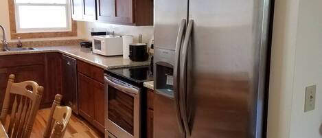 Una cocina con gabinetes de madera, un refrigerador de acero inoxidable, un microondas y una estufa.