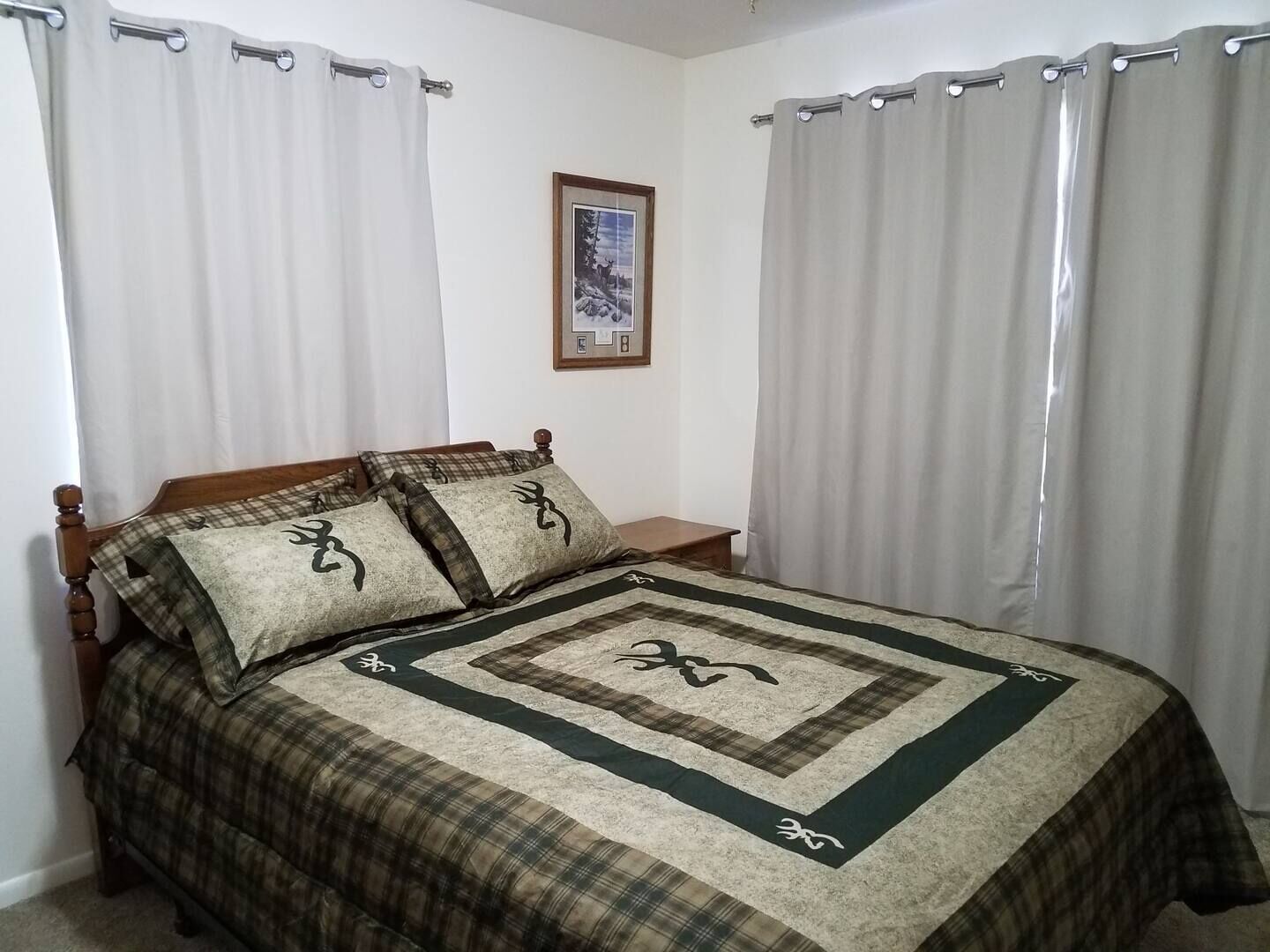 Une chambre à coucher avec un lit, des rideaux, une table de chevet et un tableau encadré au mur.