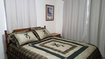 Une chambre à coucher avec un lit, des rideaux, une table de chevet et un tableau encadré au mur.