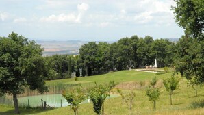 A grassy landscape with trees, a small pond, and a white structure in the distance. - Verdidea - Vallocchie (Sarteano)