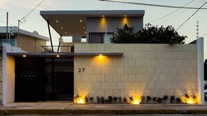 Una casa moderna con tetto piatto, ingresso carrabile e il numero '27' sulla parete.