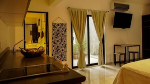 Camera d'albergo con angolo cottura, un letto, una TV e una porta scorrevole in vetro che dà sull'esterno.