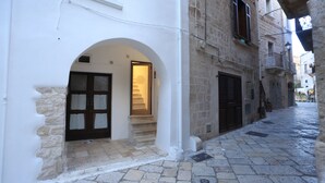 A narrow street with a white building featuring an arched doorway and a staircase leading to an upper floor. - FONTEblu b&b (Polignano a Mare)