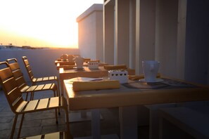 A terrace with wooden tables and chairs, a white vase, and a small card holder with heart designs. - FONTEblu b&b (Polignano a Mare)