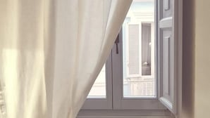 A room with a large window, white curtains, and a view of a building with shutters. - FONTEblu b&b (Polignano a Mare)