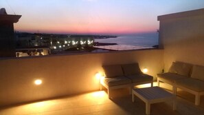 A balcony with a sofa, a small table, and a view of the sea at dusk. - FONTEblu b&b (Polignano a Mare)