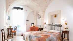 Un dormitorio con cama, escritorio, sillas y vistas a través de un arco.