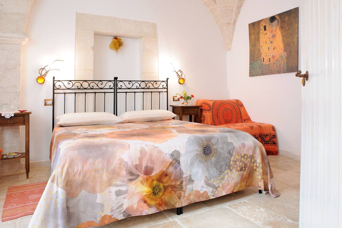 A bedroom with a bed, a nightstand, a chair, and a painting on the wall.