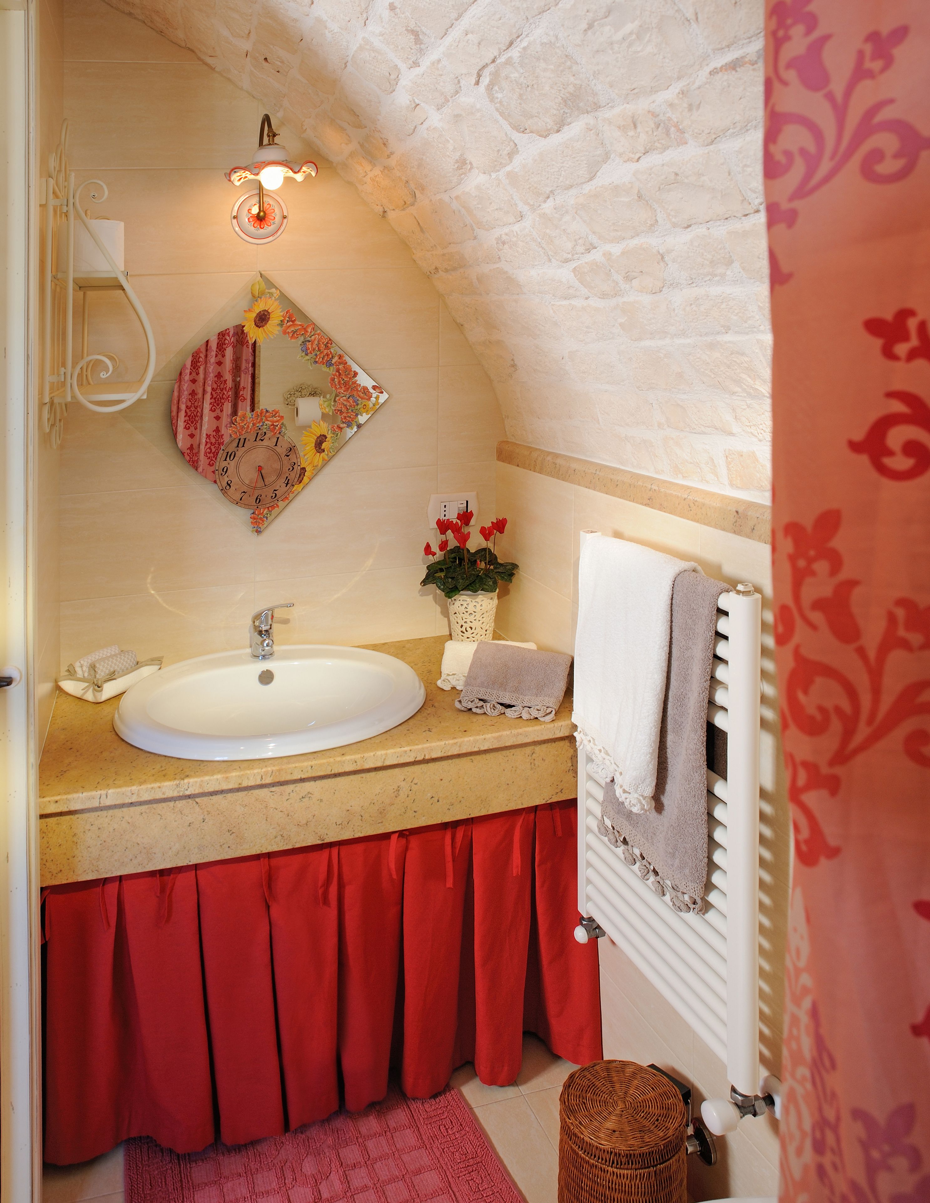 Un baño con techo de piedra, un lavamanos blanco, una toalla roja y un reloj decorativo.