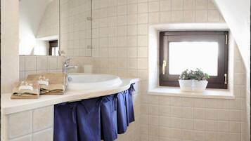 A bathroom with a white sink, a mirror, and a window with a potted plant.