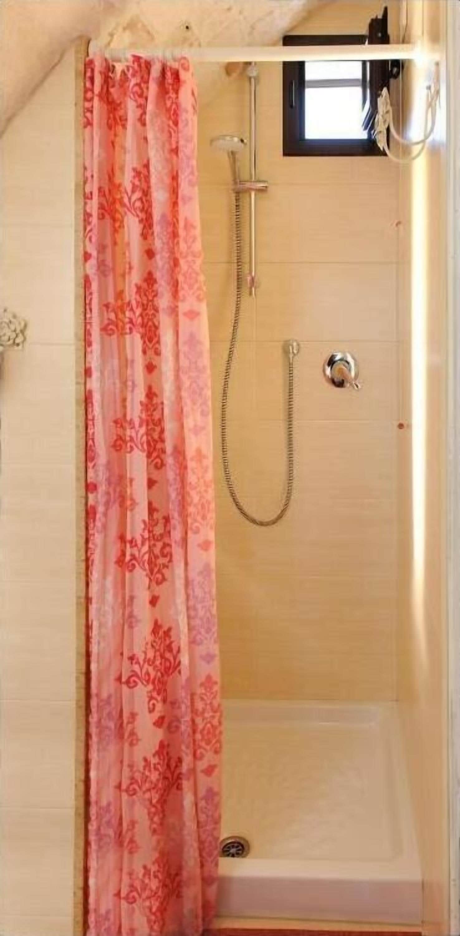 A shower area with a pink floral shower curtain, a handheld showerhead, and a bathtub.