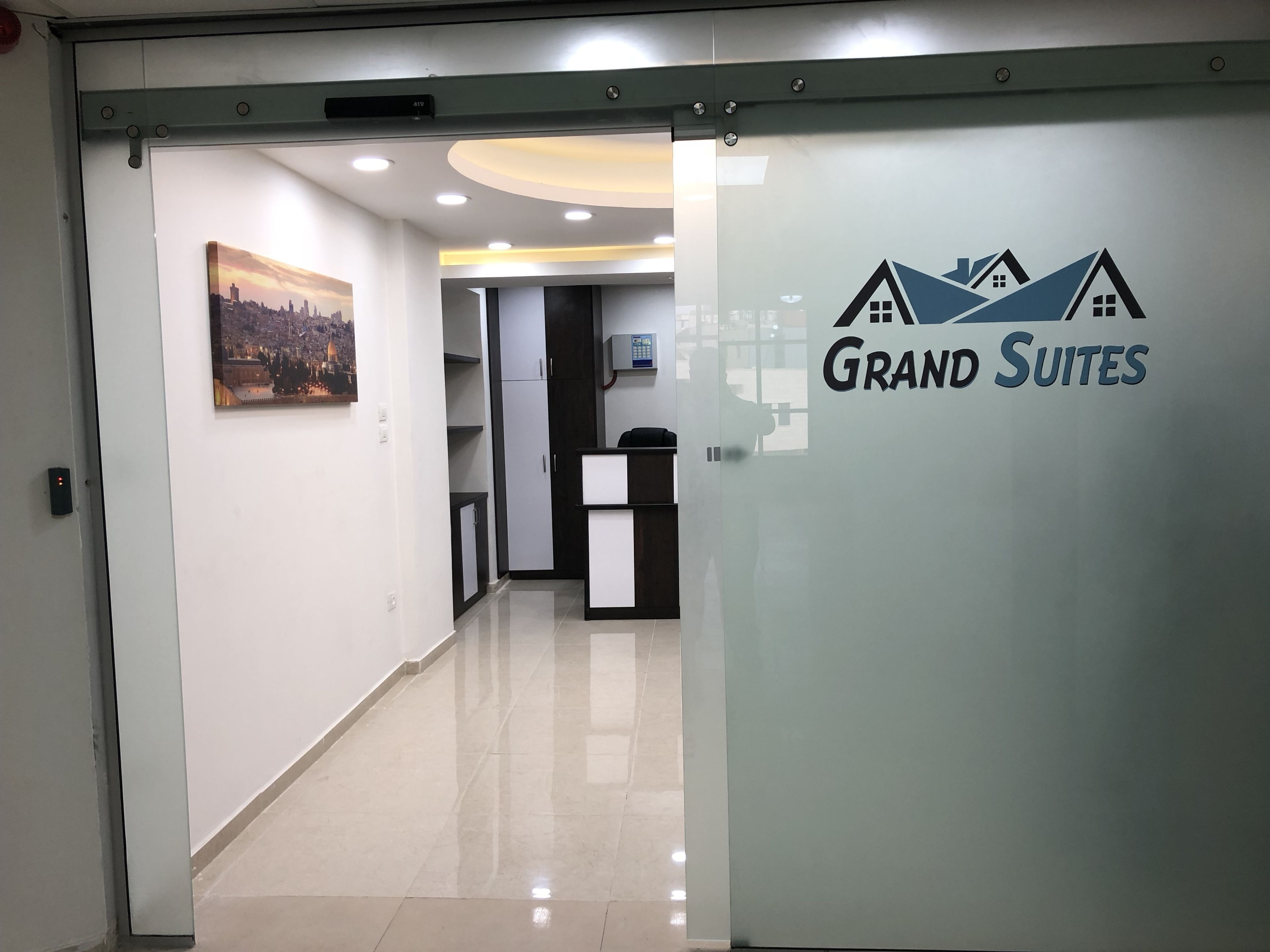 Un couloir avec un comptoir d’accueil, un tableau représentant un paysage urbain et une porte portant l’inscription « Grandes suites ».