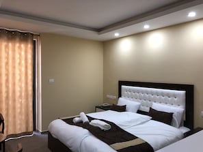 A hotel room with a large bed, a nightstand, a chair, and a window with curtains.
