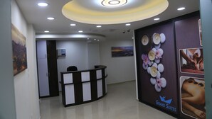 Un área de recepción con un mostrador a cuadros blanco y negro, una lámpara de techo circular y una pared con decoraciones florales e imágenes de tratamientos de spa.